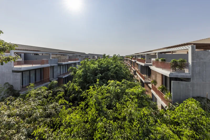 Elevated view of concrete residential blocks with planted terraces wrapped around mature tree canopy