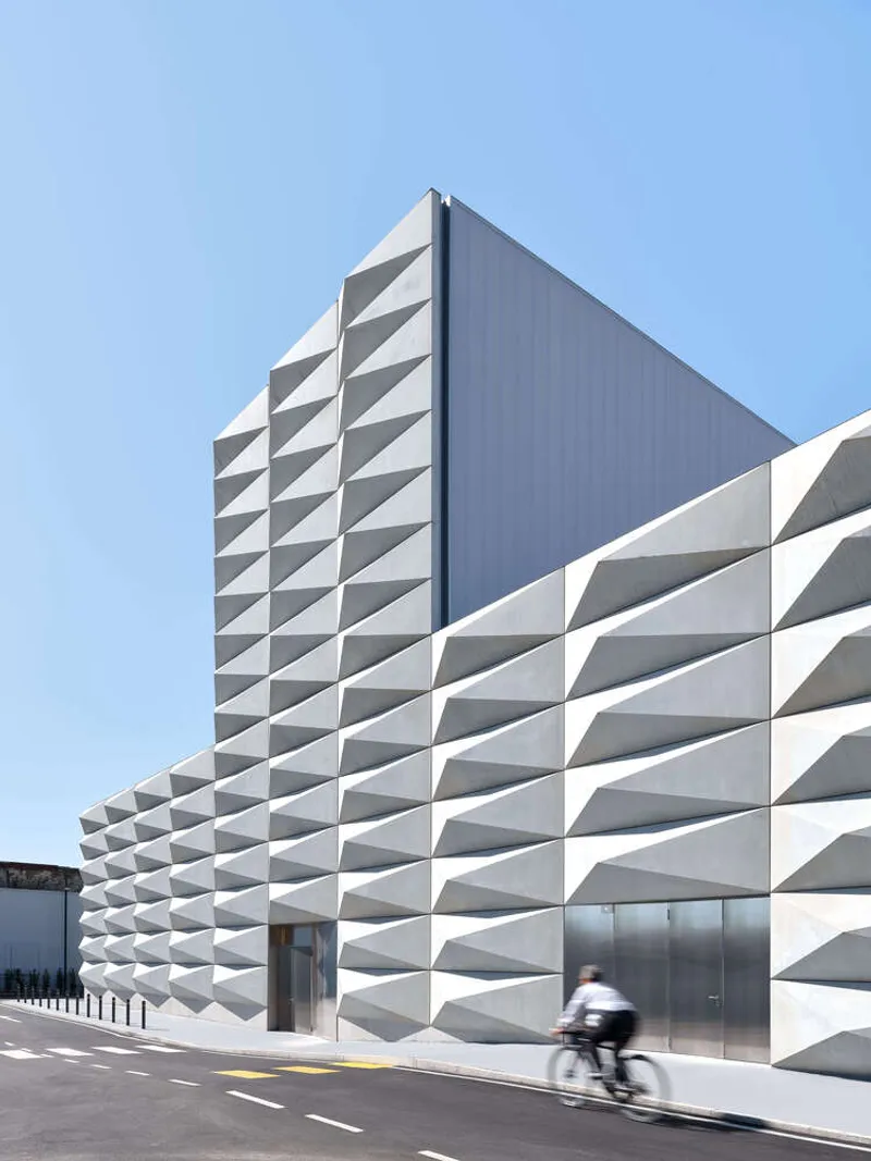 Street view of the folded white panel facade with a cyclist passing in daylight