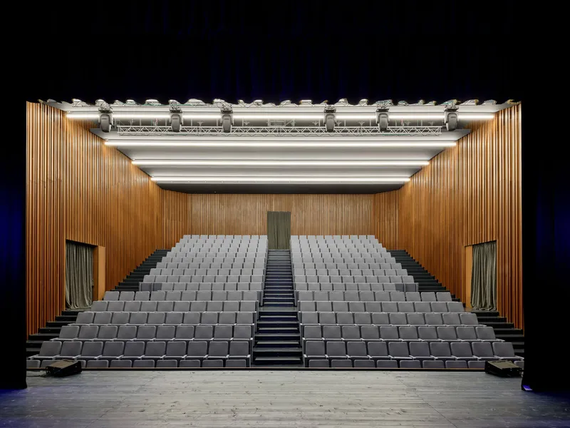 View from the stage toward the tiered auditorium seating with timber walls and exposed lighting grid
