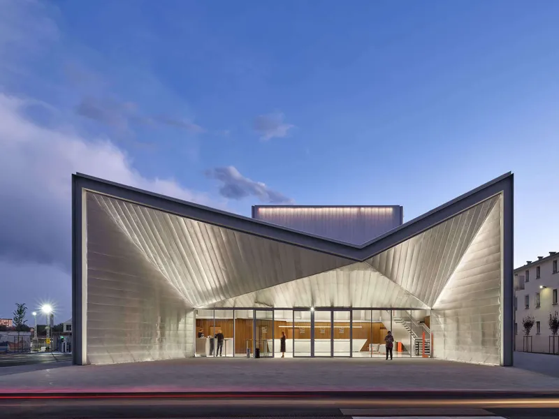 Front entrance with folded metal canopy and glazed lobby at dusk