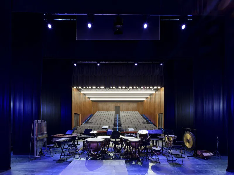 View from the performance floor toward the raised seating and timber proscenium with instruments in foreground