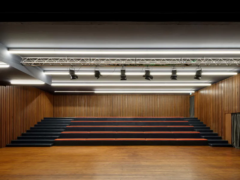 Performance hall with wood slat wall backdrop and tiered seating with black risers and orange treads