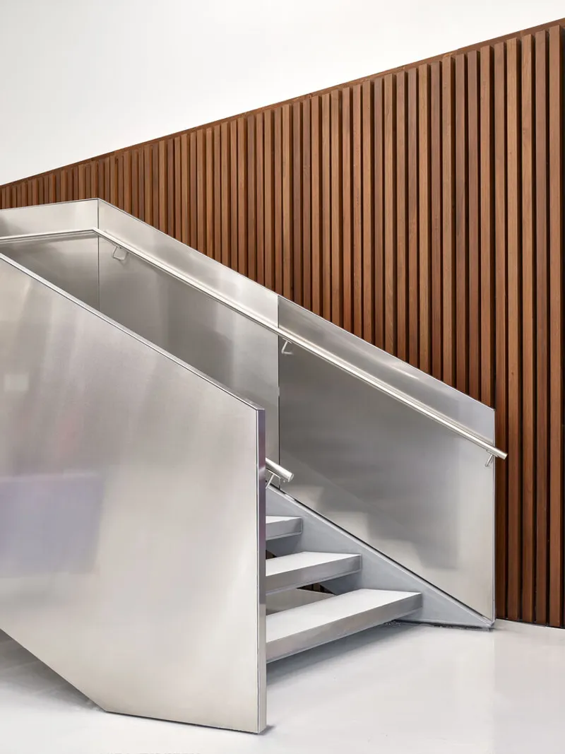 Stainless steel staircase with glass balustrade against a vertical wood slat wall