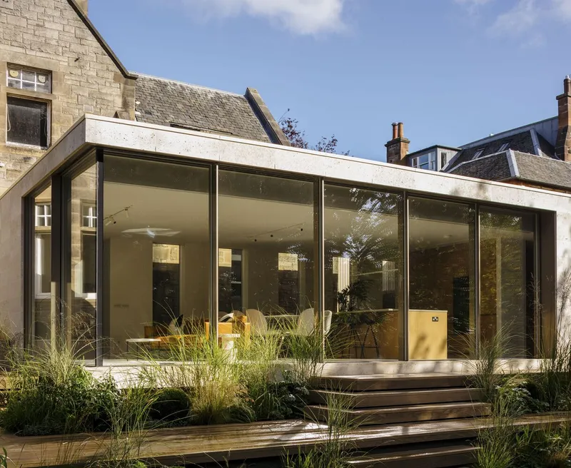 Rear garden extension with concrete roof and full-height glazed facade set among planted grasses