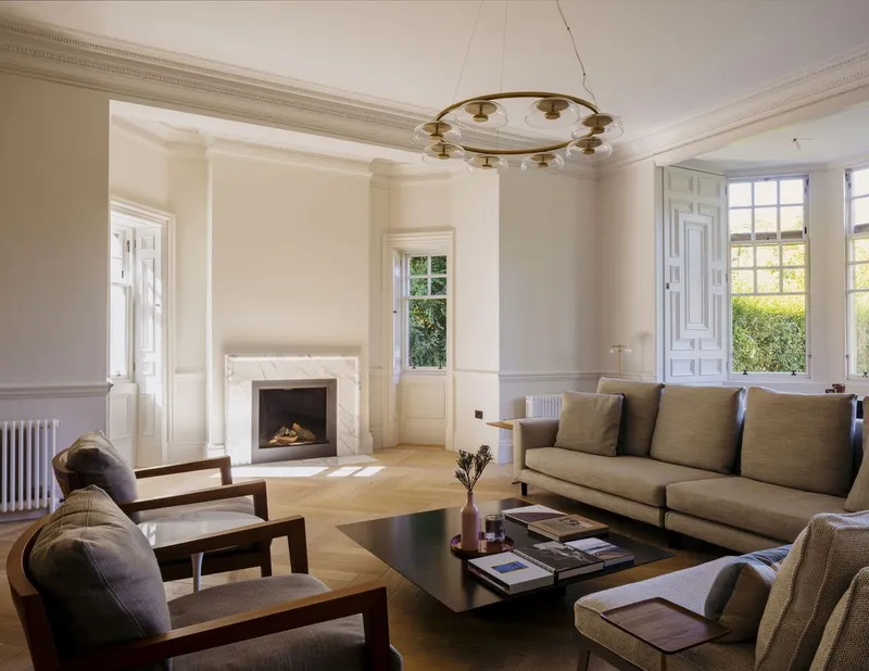 Living room with white paneled walls, fireplace, and large windows overlooking greenery
