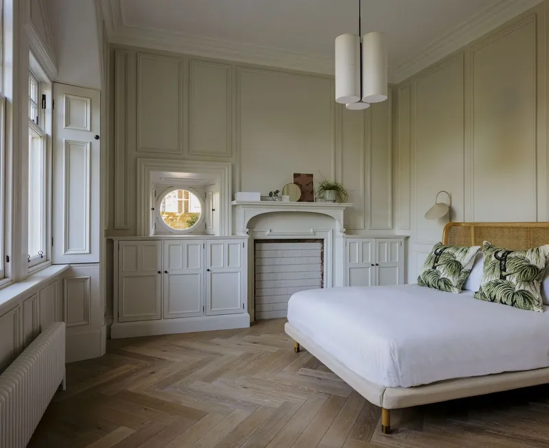 Bedroom with paneled wall cabinetry, circular window, fireplace mantel, and herringbone wood flooring in daylight