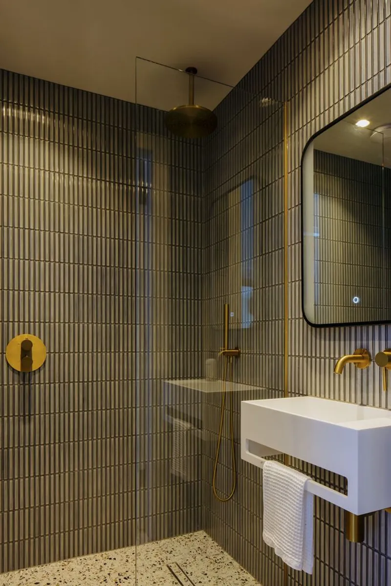 Bathroom with vertical fluted tile walls, brass fixtures, glass shower enclosure, and terrazzo flooring