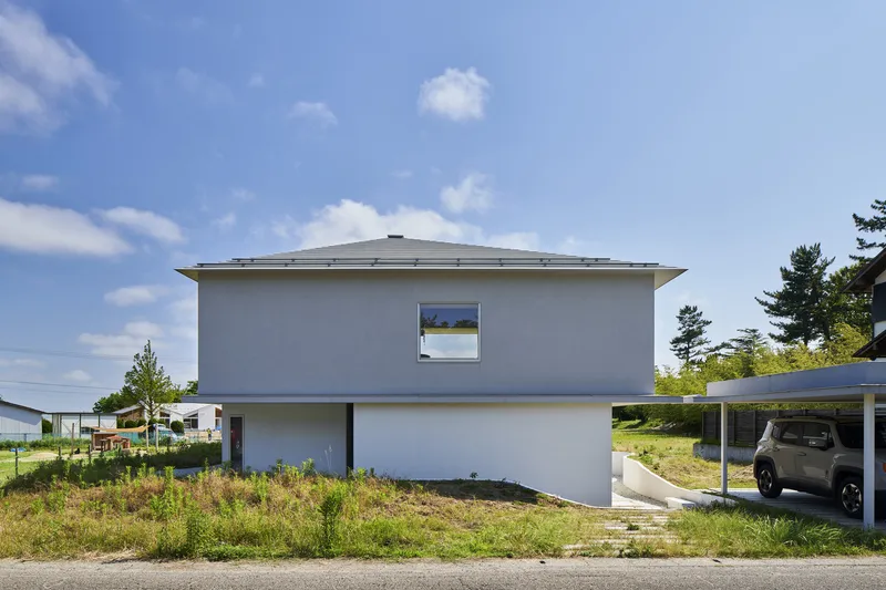 Street view of the white rendered facade with shallow hipped roof under blue sky