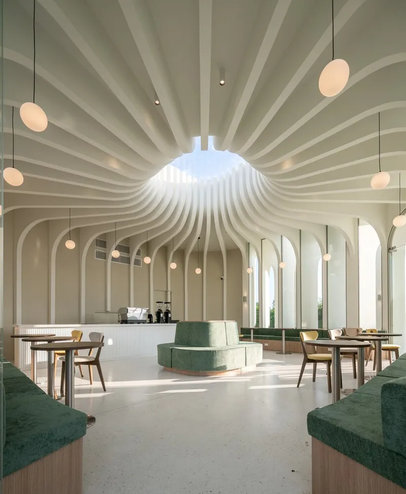 Interior space with radiating ribbed ceiling and pendant globe lights above green upholstered seating