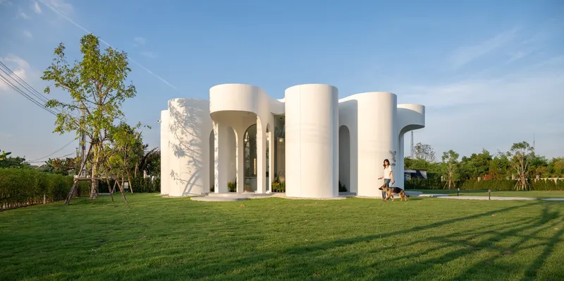 White cylindrical volumes grouped around a central void on a lawn in afternoon light