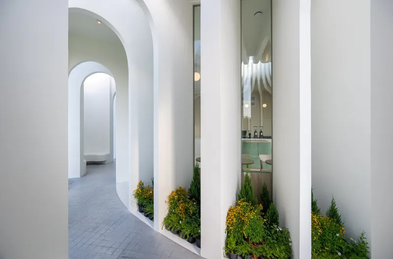 Curved corridor with planted beds of conifers between the white cylindrical columns