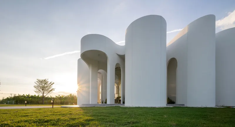 White cylindrical volumes with arched openings surrounding a lawn at sunset
