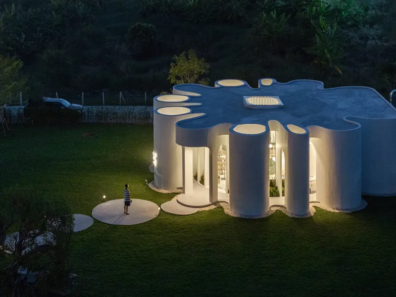Aerial night view of the illuminated building with circular roof openings and a figure on the lawn