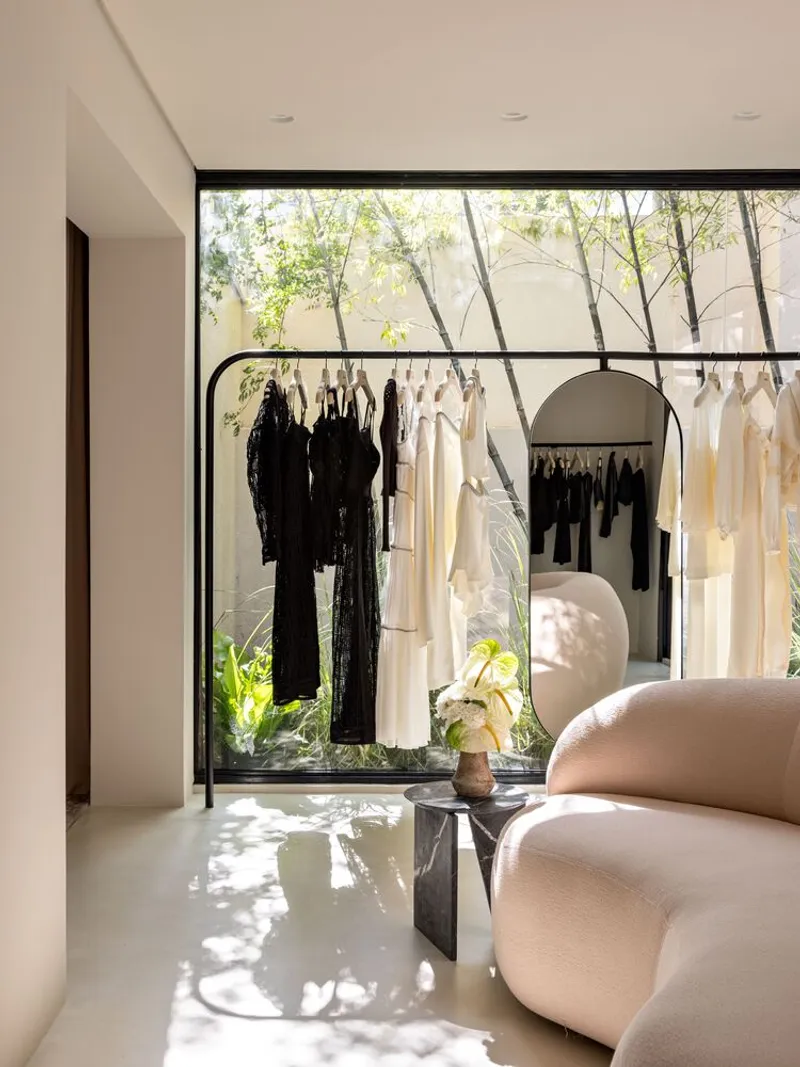 Retail display space with black metal garment rack beneath a clerestory window overlooking a planted courtyard