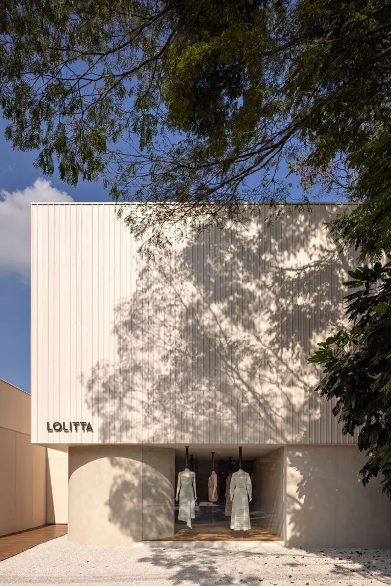 White corrugated metal facade with arched entry beneath dappled tree shadows