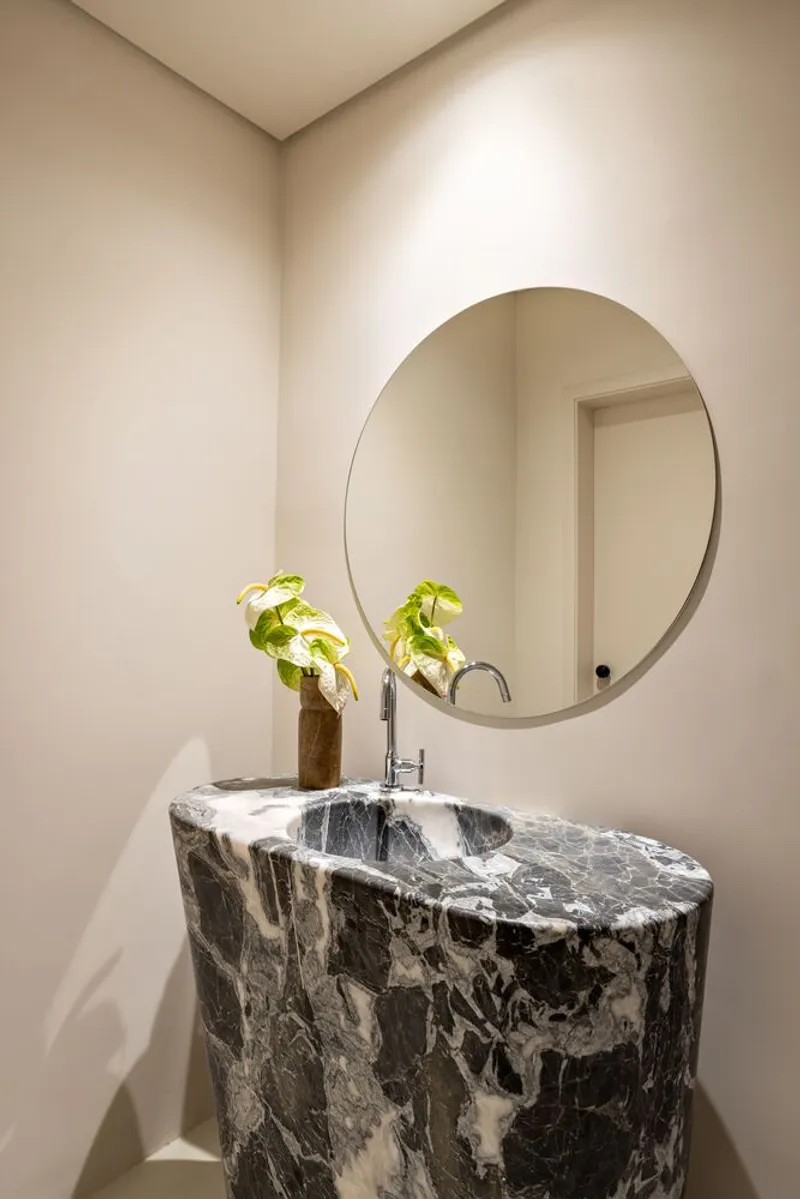 Cylindrical black and white marble vanity beneath a circular mirror in a powder room