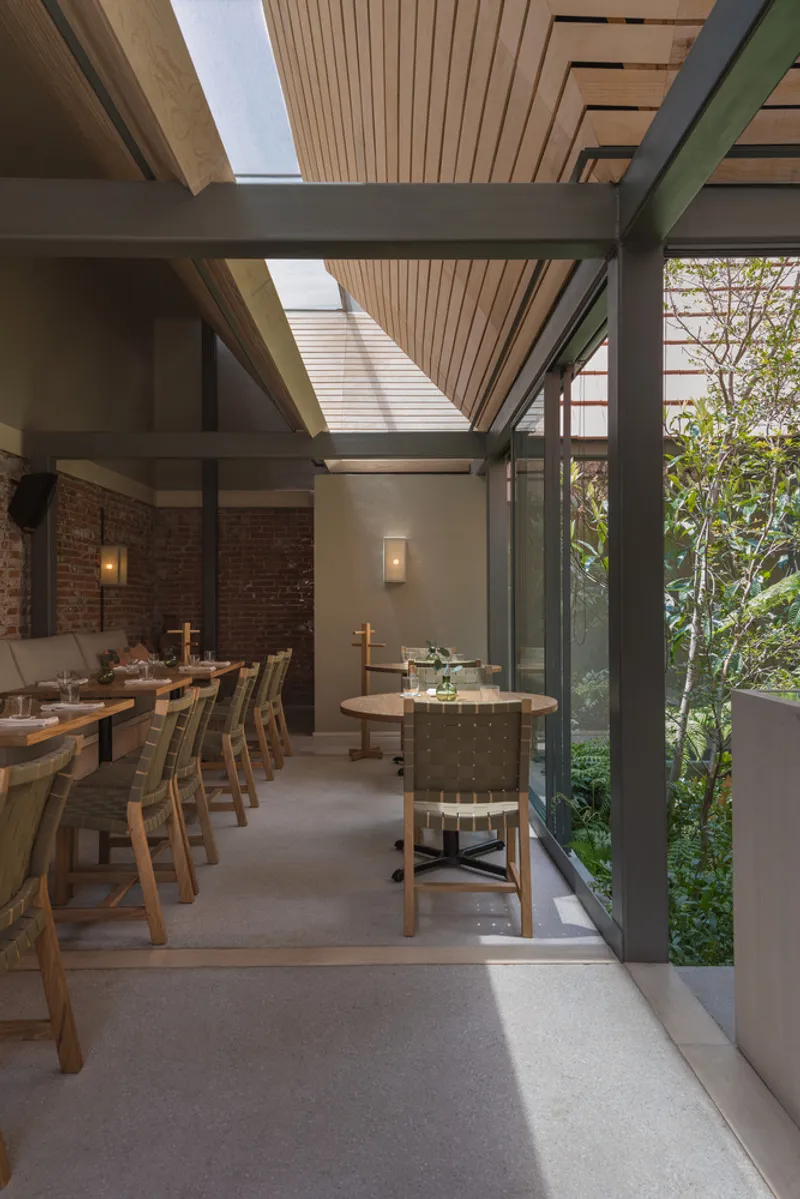 Dining area with slatted timber ceiling, steel beams and glazed wall opening to a planted courtyard
