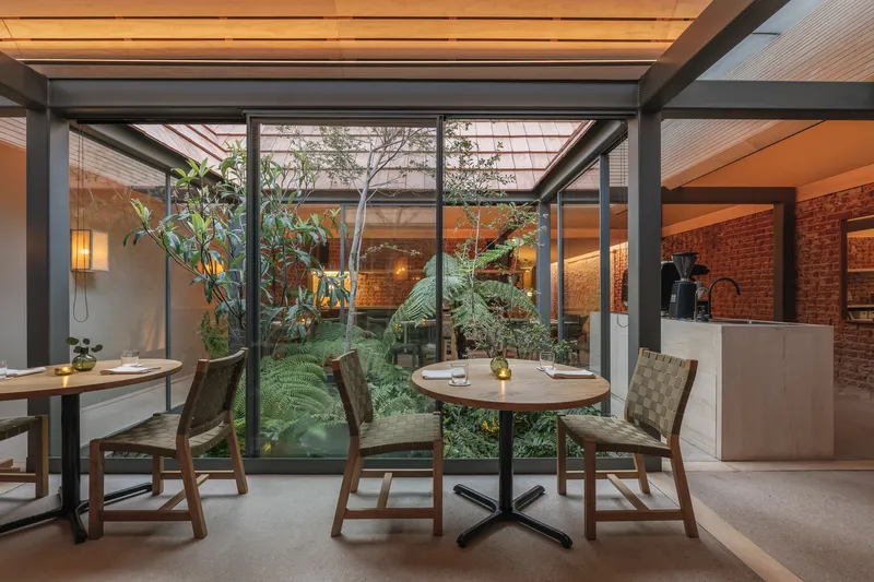 Seating area overlooking an interior courtyard garden framed by steel columns and glazing at dusk