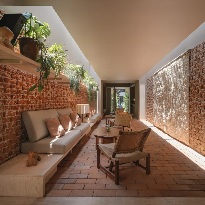 Interior corridor with exposed brick walls, terracotta tile floor and dappled sunlight filtering through skylights