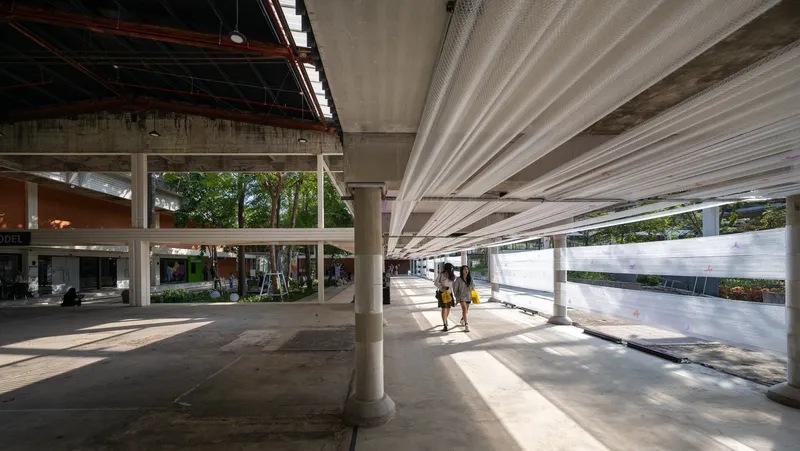 View along the concrete floor with cylindrical columns and fabric screens filtering afternoon sunlight