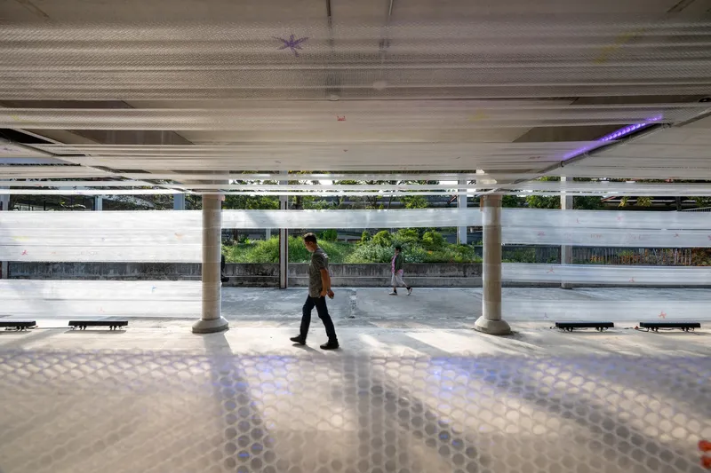 Patterned floor reflecting light from the perforated ceiling as a pedestrian crosses the open plaza