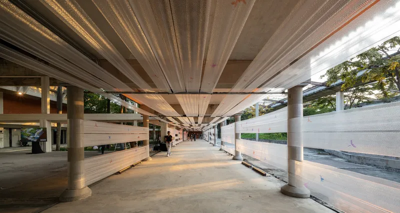 Corridor at dusk with warm interior lighting visible through glazing and the pleated ceiling overhead