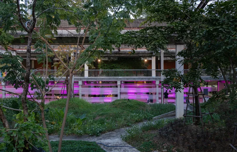 Magenta-lit horizontal screening panels beneath a concrete deck framed by trees at dusk