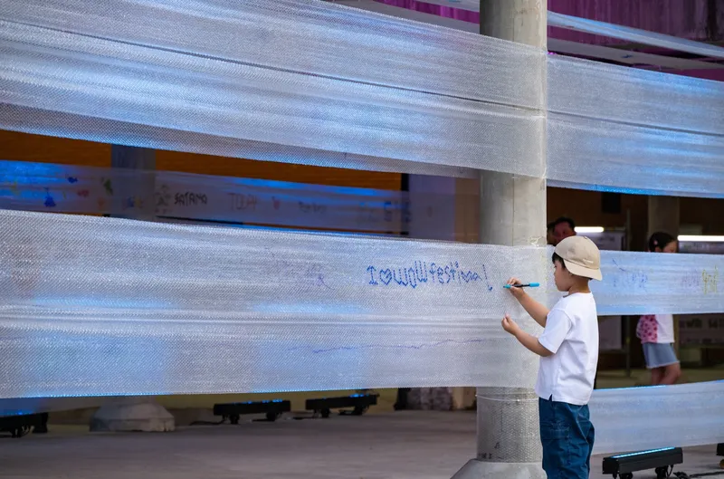 Child writing on translucent horizontal mesh screening wrapping a concrete column