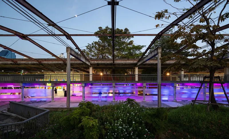 Central courtyard with steel truss canopy above magenta-illuminated screening and planted landscape at dusk