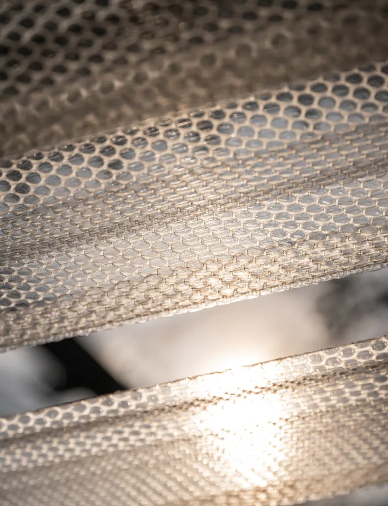 Close-up of layered perforated metal panels with dappled sunlight creating shadow patterns