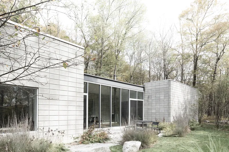 Glazed courtyard entrance flanked by white-tiled volumes and naturalistic planting with grasses and boulders