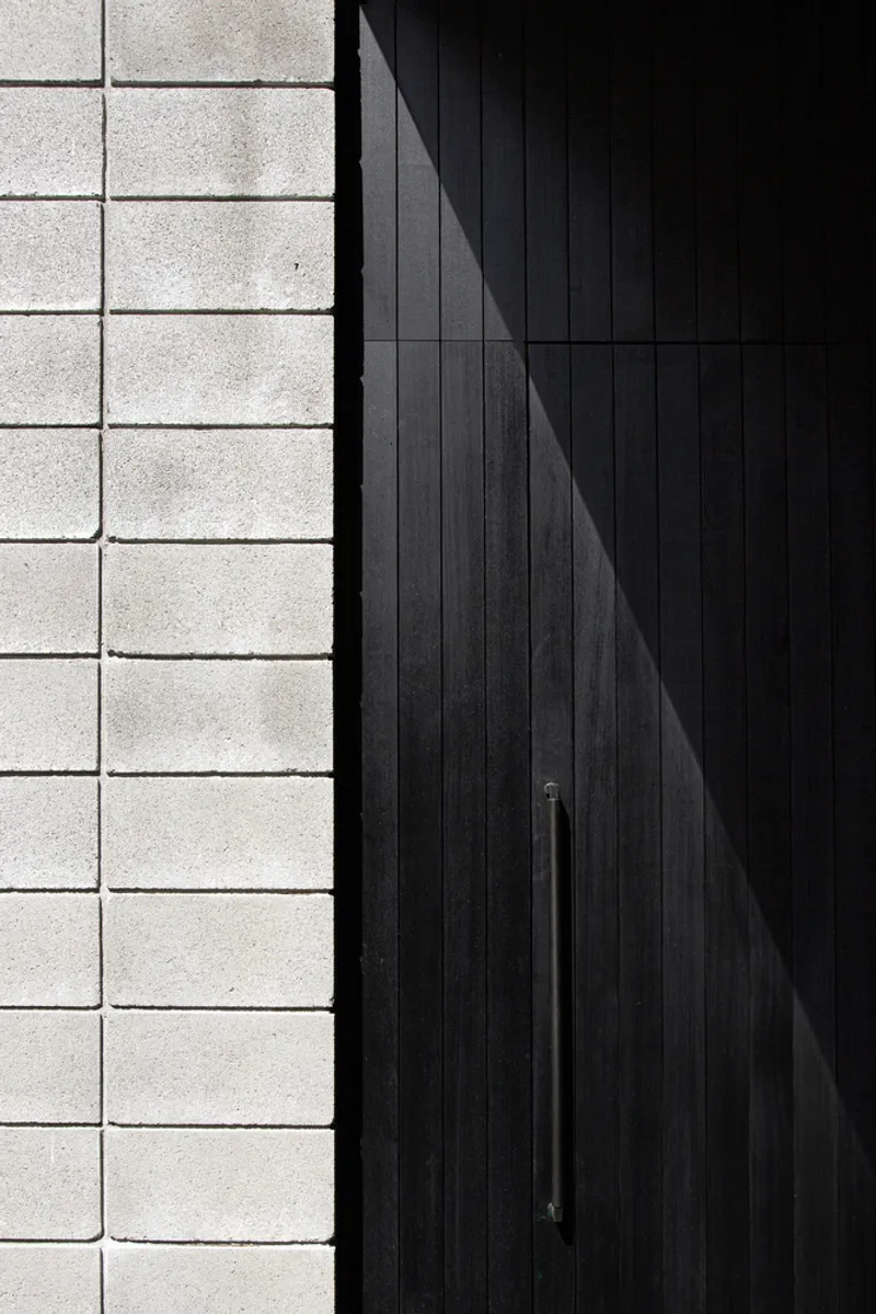 Detail of black vertical timber cladding meeting light grey concrete block wall in direct sunlight
