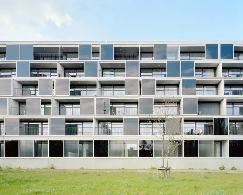 Grid facade of recessed balconies with sliding glass and opaque panels fronting a grassed lawn with young tree