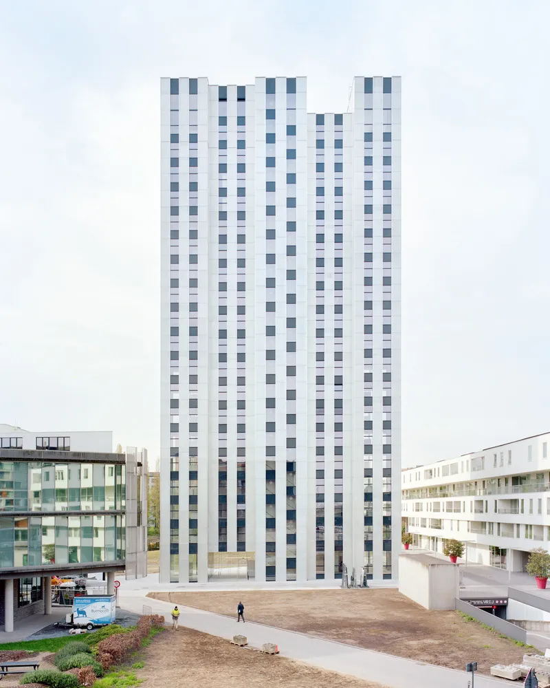 Residential tower with vertical stripes of white and grey window panels rising above an open plaza