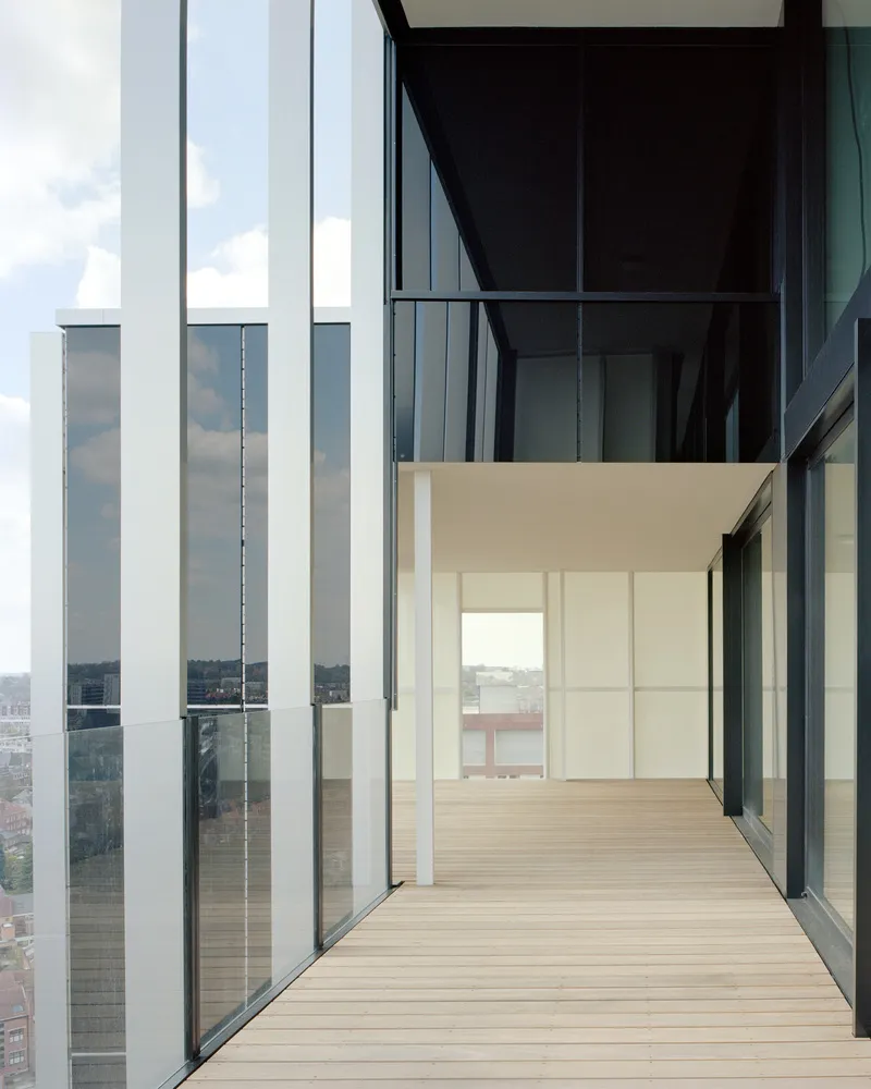 Timber-decked balcony framed by vertical white fins and floor-to-ceiling glass with city views beyond