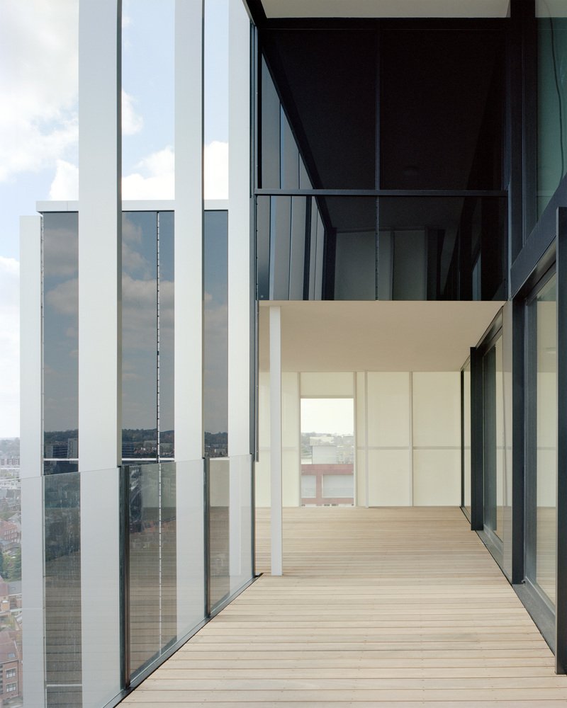 Timber-decked balcony framed by vertical white fins and floor-to-ceiling glass with city views beyond
