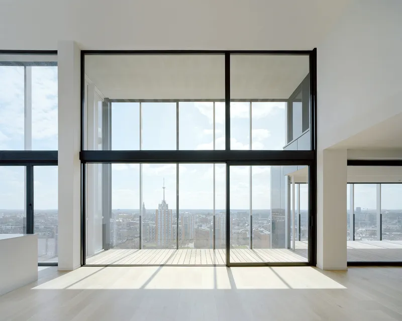 Double-height interior space with full-height glazing opening onto a timber balcony framing distant tower