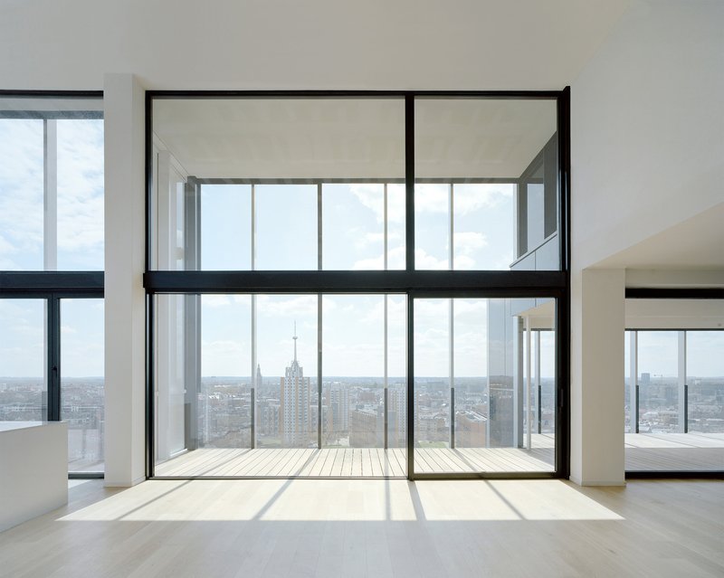 Double-height interior space with full-height glazing opening onto a timber balcony framing distant tower