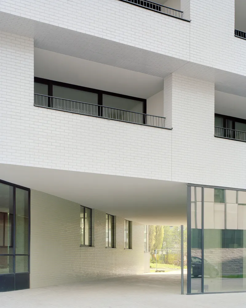 View into the covered entrance loggia showing white brick walls and deep cantilevered balconies above