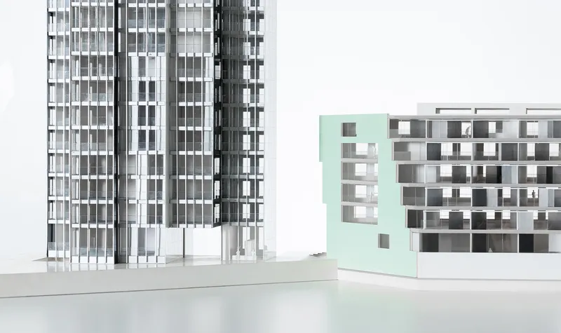 Physical model showing a slender tower and a lower mint-green volume with perforated facade openings