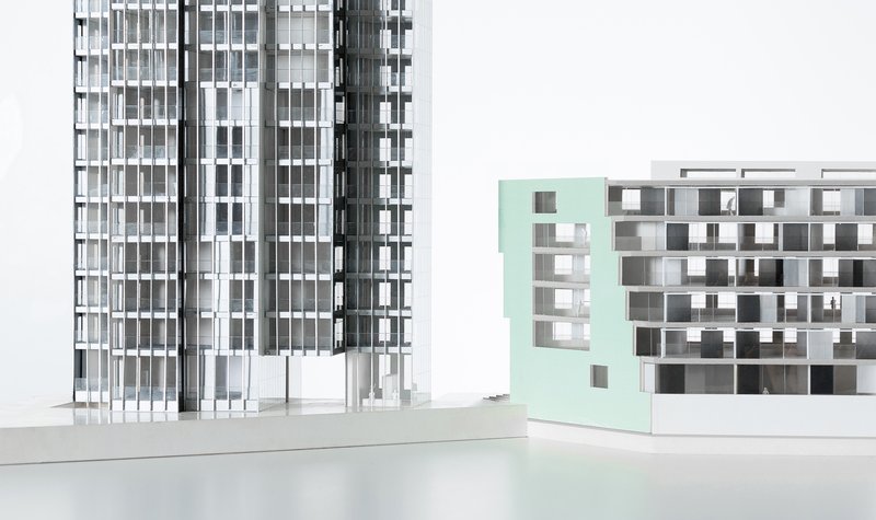 Physical model showing a slender tower and a lower mint-green volume with perforated facade openings