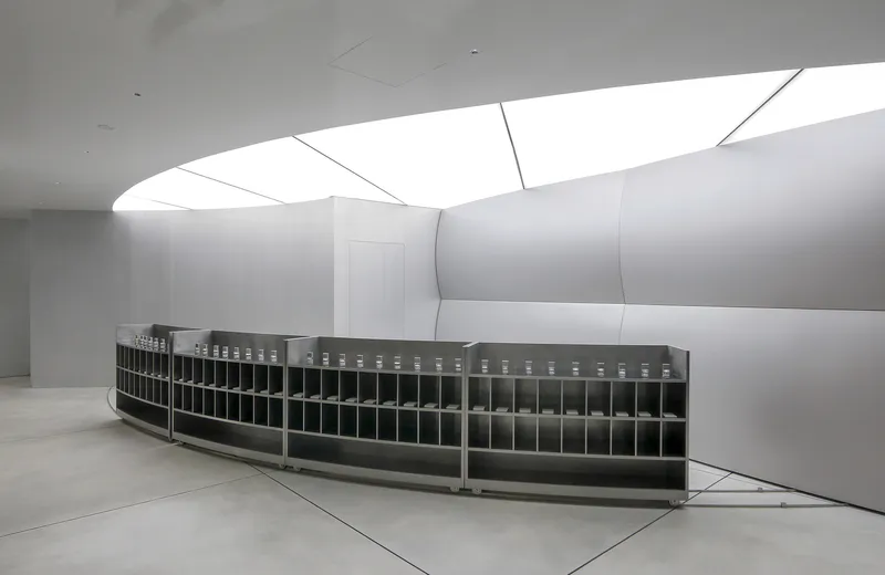 Curving reception counter with gridded compartments beneath angular skylights in a white interior