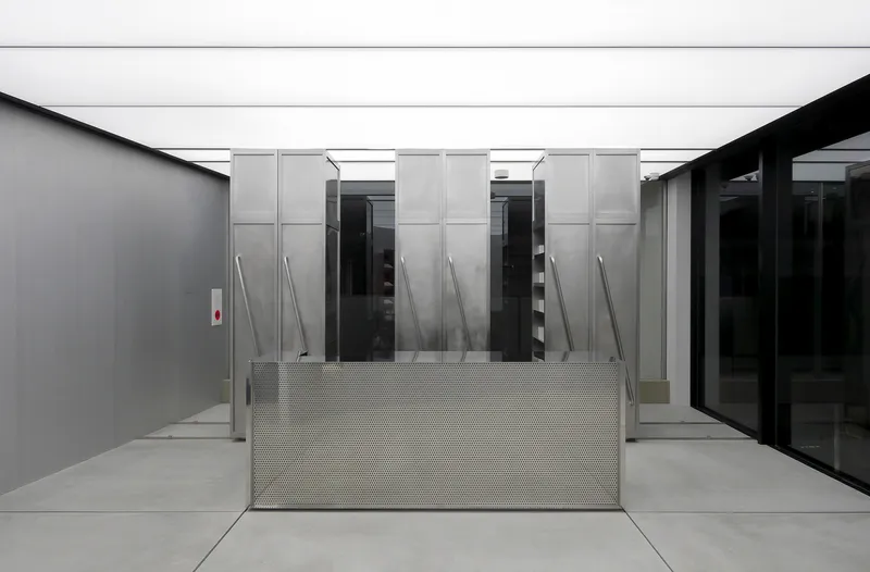 Metal access ramp with perforated guardrail leading to translucent sliding panels and elevator banks