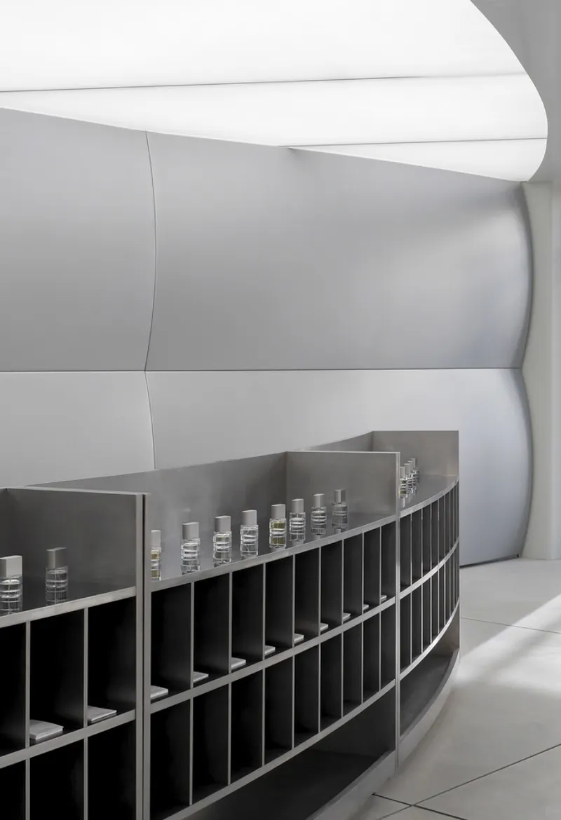 Curved shelving unit with product bottles displayed in gridded compartments along a white wall
