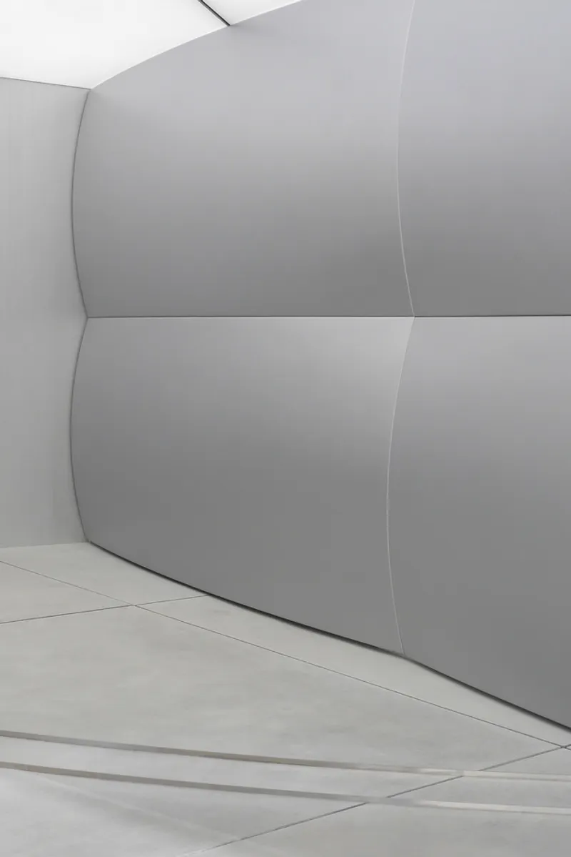 Detail of curved white wall panels meeting at a vertical seam above tiled flooring