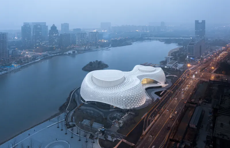 Aerial view of the white perforated roof beside a lake and highway at dusk