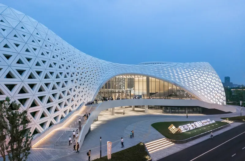 Entry plaza with triangulated white facade and glass entrance at twilight