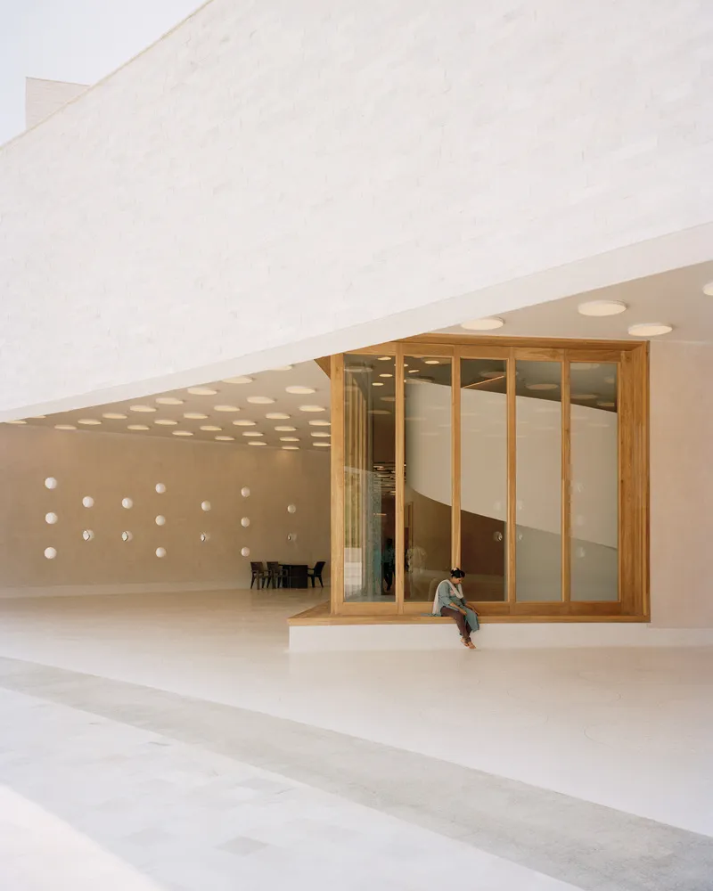 Ground-level view of timber-framed pavilion with glass walls and a single seated visitor on the ledge