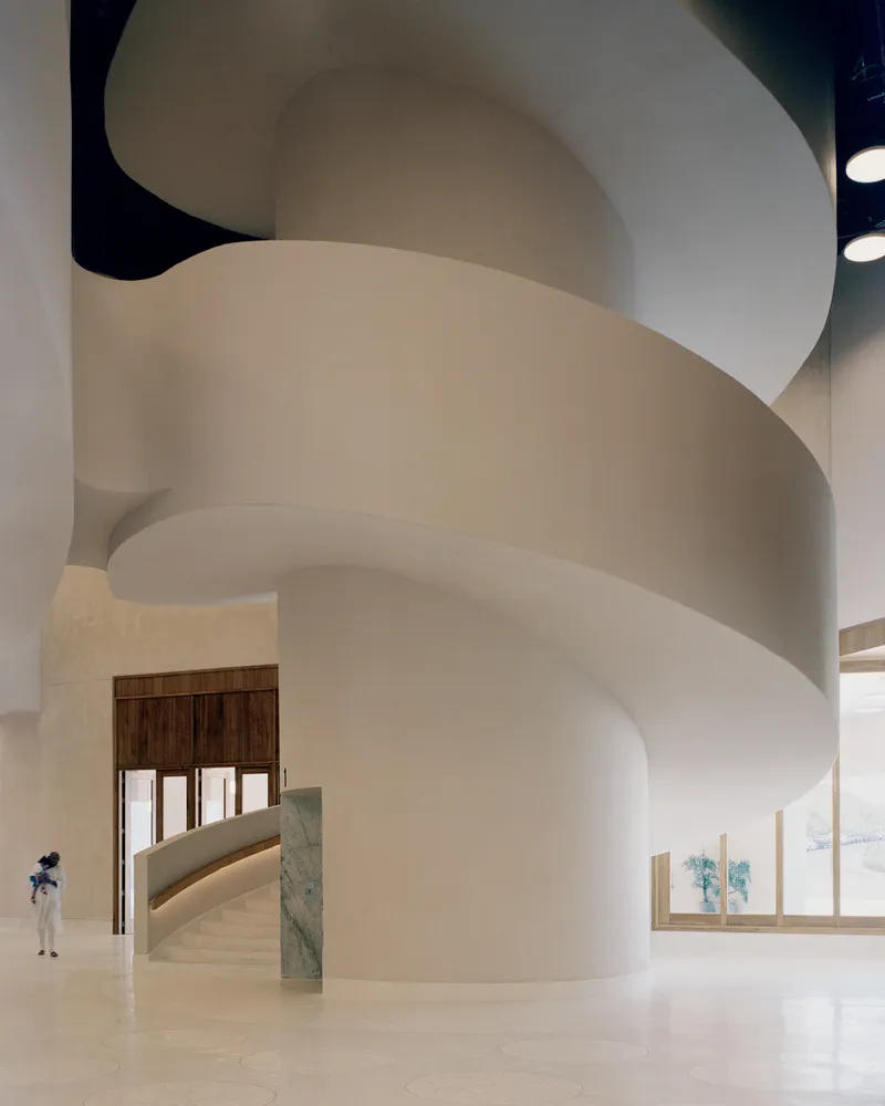 Spiraling white staircase with polished terrazzo flooring and a figure standing near the timber entry doors
