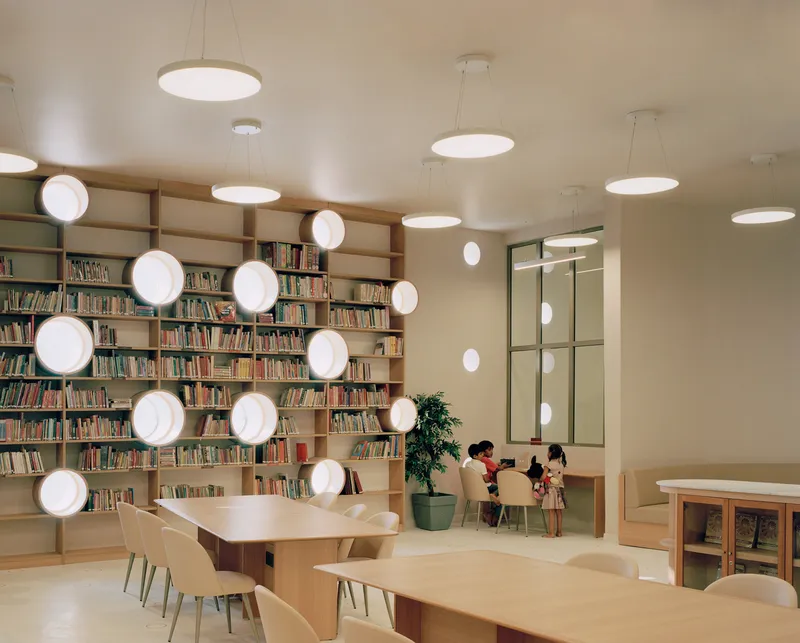 Reading room with timber shelving, circular pendant lights, and children seated at pale wood tables